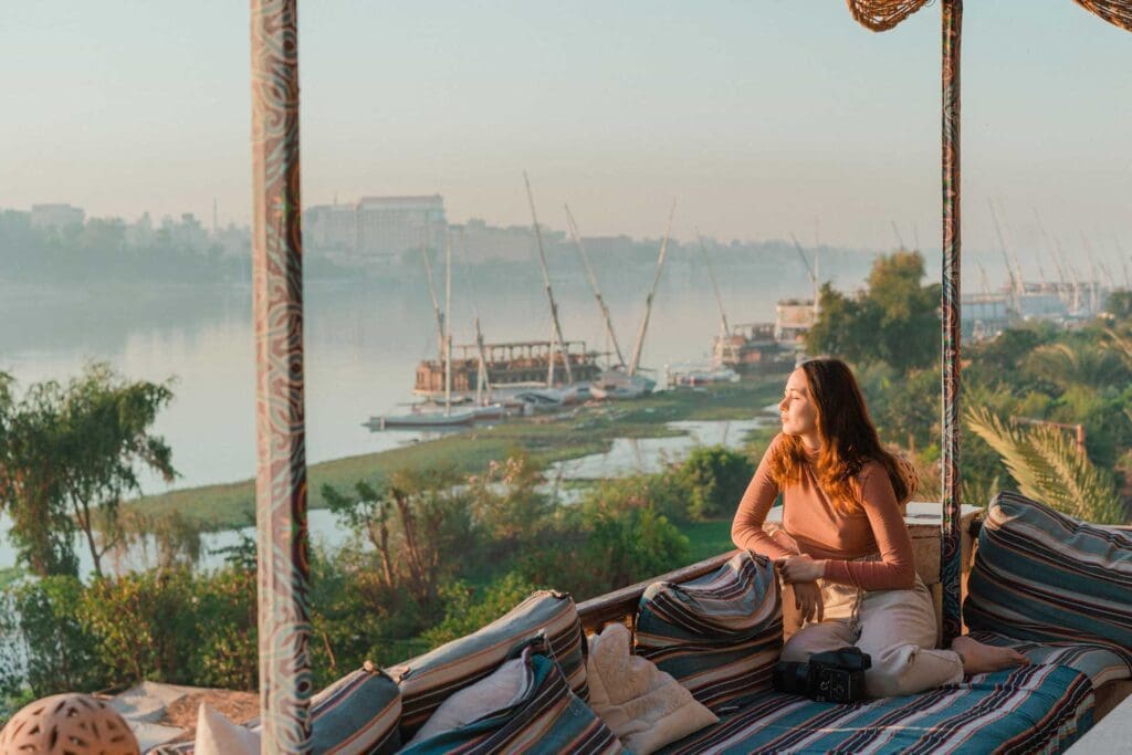 A woman sitting on top of a couch looking out at the water.