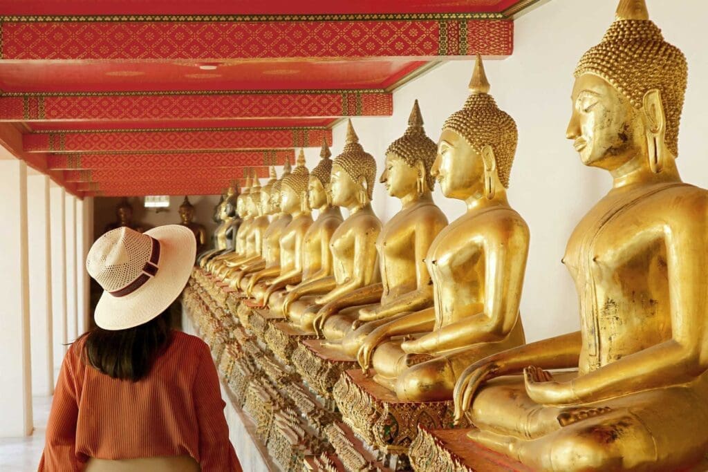 A woman in a hat standing next to many gold statues.