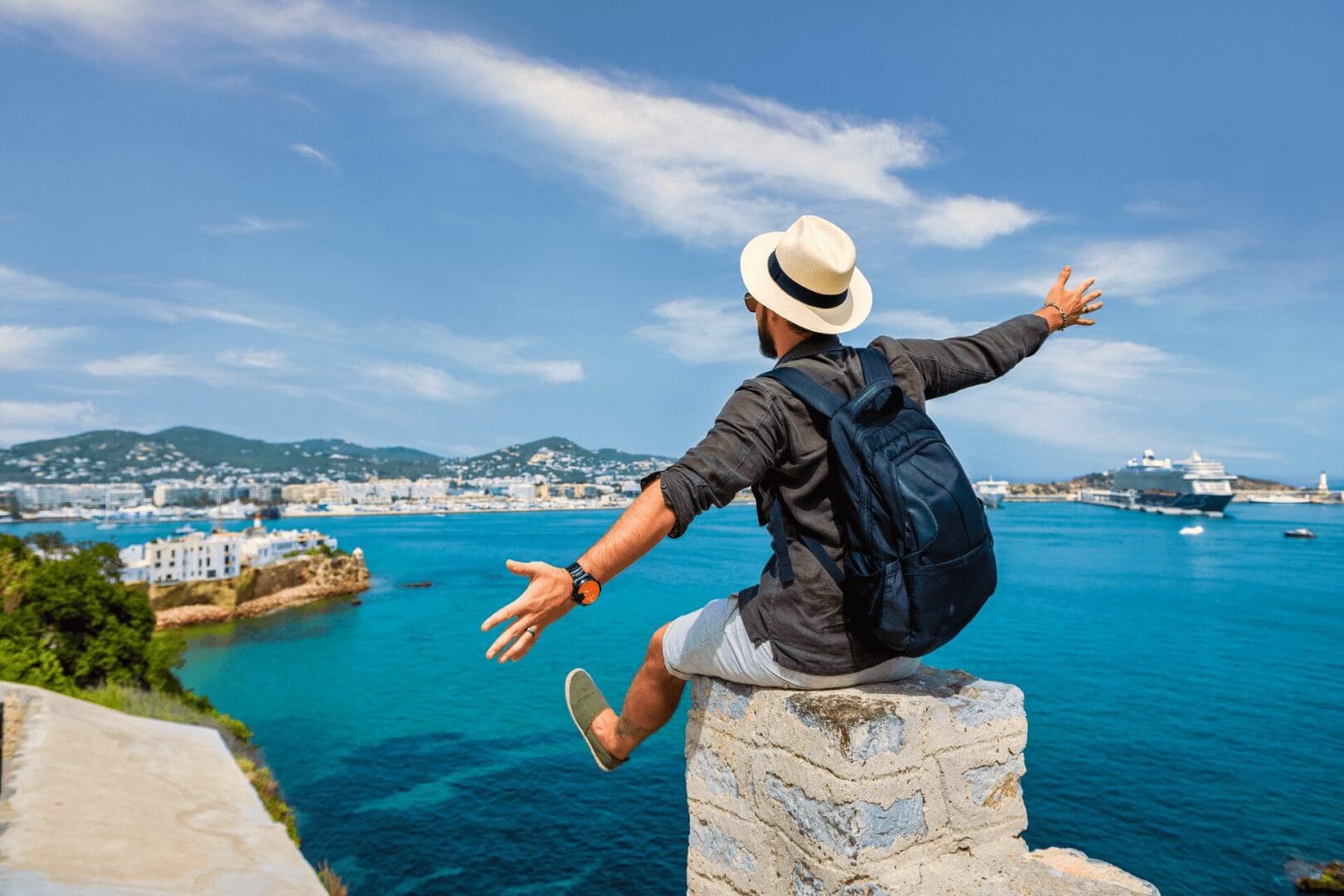 A man with his arms outstretched sitting on top of a stone wall.